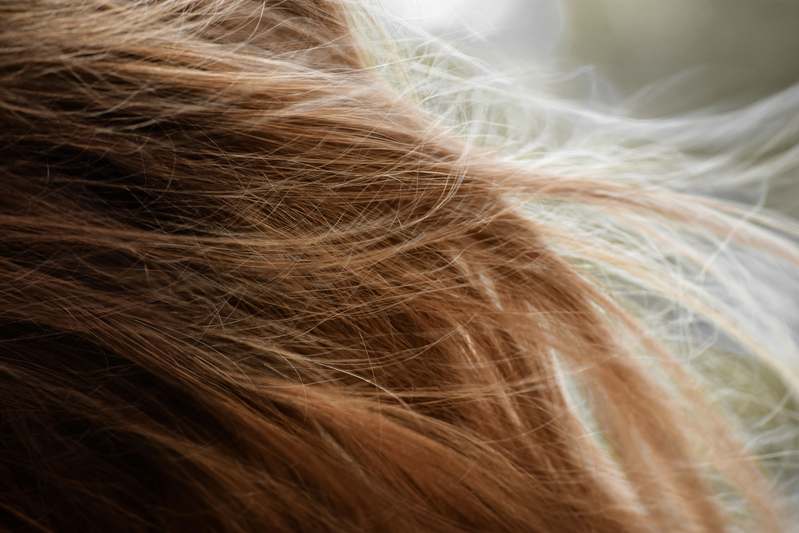 Close-up of a hand holding a matte-finish hair spray bottle with subtle golden branding, on a soft beige linen background