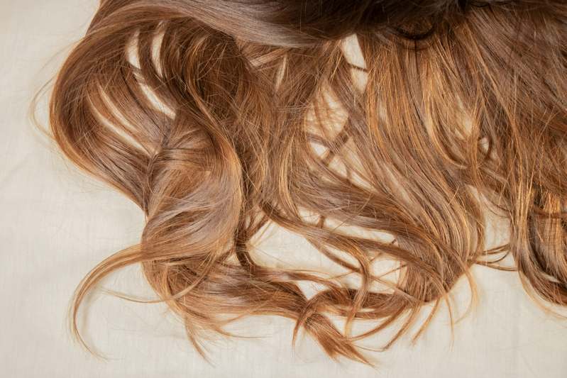 Professional hairstylist mid-application of flexible-hold hair spray on textured wavy hair under natural daylight
